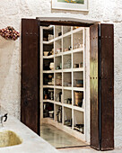 Offene Holztüren mit Blick auf weißes Küchenregal mit Geschirr und Kochuntensilien