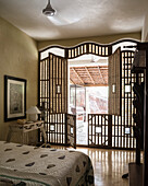 Schlafzimmer mit dekorativem, geschnitztem Holzraumteiler und Blick ins Freie
