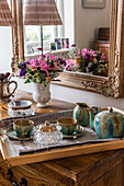 Tablett mit Teeservice und buntem Blumenstrauß auf antiker Holzkommode