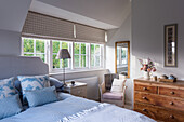 Schlafzimmer mit grauem Polsterbett, hellblauer Bettwäsche und Holzkommode
