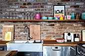 Wooden shelf with colorful bowls above kitchen worktop on brick wall