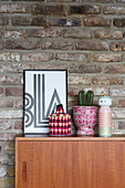 Wooden sideboard with decoration in front of brick wall