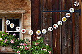 DIY-Girlande aus runden Platten mit Blumen an Holzwand im Außenbereich