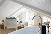 Freestanding bathtub in the attic bedroom with wooden floor and rattan furniture