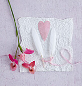 Two white feathers tied with a ribbon with a pink heart between them and orchid flowers (partnership and sexuality)