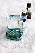 Grobes Salz mit Löffel in einem Döschen, ätherische Öle im Hintergrund (für ein Salzbad)
