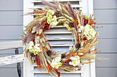 Autumn wreath made of dried flowers and berries on vintage window shutter