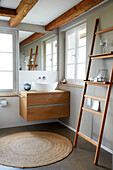 Wooden washbasin and decorative ladder in the bathroom with rattan rug