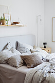 Bed with light-colored linens and wall shelf with plant in the bedroom