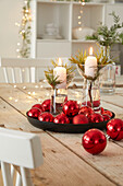 Christmas table decoration with candles and red baubles on a wooden table