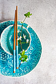Türkisblaues Frühlingsgedeck mit Keramikgeschirr, Essstäbchen und blühendem Kirschzweig