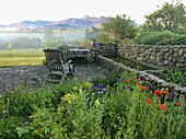 Landhaus-Terrasse mit Sitzgruppe, Blumenbeeten und Wasserbecken mit Natursteinmauern