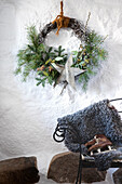 Weihnachtskranz an weißer Wand über rustikalem Kamin mit Schaffell