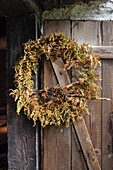 Getrockneter Herbstkranz aus Farn und Beeren an rustikaler Holztür