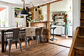 Open-plan cooking and dining area, woman in green dress in kitchen, rustic living style