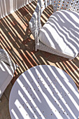 White garden table and rattan chairs with cushions on terrace with shade pattern