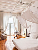 White bedroom with canopy bed, curtains and wooden floor