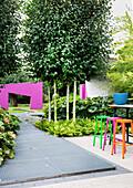 Gartenplatz mit bunten Barhockern, im Hintergrund pinkfarbener Mauer mit Durchgang (Appeltern, Niederlande)