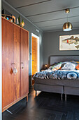Teakholz-Schrank und Doppelbett im Schlafzimmer mit schwarzem Fischgrätparkett