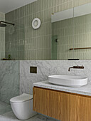 Vanity unit with countertop basin and toilet in a bathroom with green tiles and marble tiling