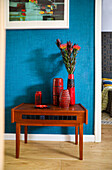 Schränkchen mit Vasen und Blume vor Wand mit blauer Tapete