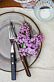 Frühlingsgedeck mit lila Fliedern auf Tisch im Freien