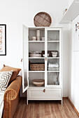 White glass door cabinet with crockery next to a rattan sofa