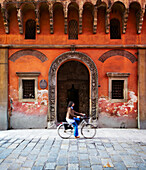 Fahrradfahrerin vor verfallener Fassade eines Palazzo (Bologna, Italien)