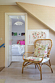 Landing with patterned wallpaper and rattan chair, looking into the bedroom