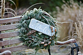 Winterkranz aus verschiedenen Tannengrün, dekoriert mit Zapfen und einem Holzschild mit der Aufschrift 'Winter'