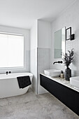 A modern double ensuite bathroom in monochromatic décor with white subway tiles, black tapware and black joinery. A freestanding bath is in the background.