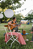 Woman playing guitar under tree with pennant chain and lanterns