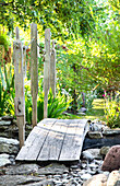 Bogenbrücke aus Holz über Bachlauf im Garten
