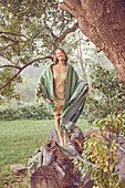 Young woman with various blankets in shades of green standing on a log