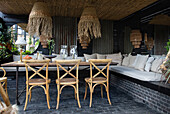 Robust boho table with chairs and bench, above sea grass lamps on covered terrace