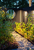 Zaun mit rundem Spiegel im beleuchteten Garten