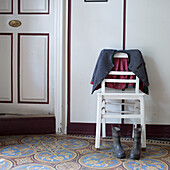 White-painted wooden chair with jacket and wellington boots on a colourful tiled floor