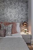 Double bed with pillows and bedside table in front of monochrome wallpaper