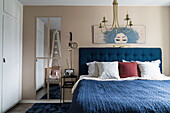 Blaues Bett mit blauer Tagesdecke im hellen Schlafzimmer in Beigetönen