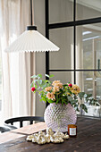 Bouquet of flowers in a decorative vase on a wooden table, pendant light above it