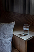 Ein Glas Wasser auf dem Nachttisch hinter dem Bett