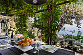 Gedeckter Tisch mit Zitrusfrüchten und cremefarbenen Rosen auf der Terrasse mit Meerblick