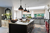 Bespoke kitchen island with industrial style pendant lights above in open plan kitchen with multi colored slate floor