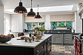 Custom made kitchen island, industrial style pendant lights above it in an open kitchen with colorful slate floor