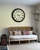Oversized wall clock above an antique French rattan sofa