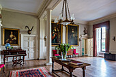 Tisch, Klavier und großformatige Goldrahmen-Gemälde im Empfangsraum eines Landhauses