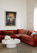 Brick red sectional corner sofa, paintings hung on the wall, white designer coffee table in the foreground