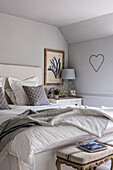 Unmade bed in a cottage room with heart decoration on the wall