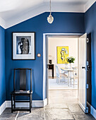 View through blue entrance hall to bright and airy dining room. A James Wedge painting hangs at the far end. the ceiling light is Immy by Laura Ashley
