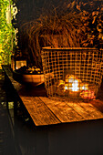 Illuminated metal basket on wooden table in garden